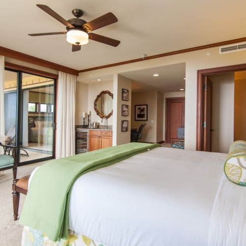 A cozy bedroom with a large bed, ceiling fan, and balcony access; features warm tones and modern decor.