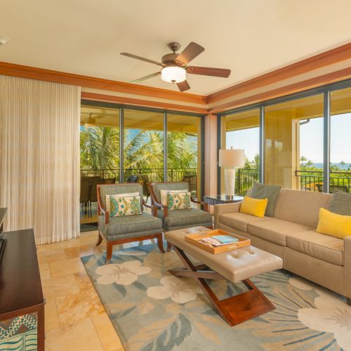 A cozy living room with a sofa, armchairs, table, TV, and large windows opening to a balcony with greenery outside.