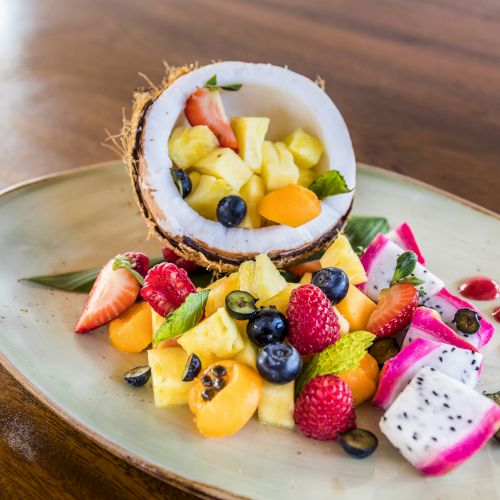 A plate with assorted fresh fruits, including strawberries, dragon fruit, and a halved coconut filled with diced fruit, displayed artfully.