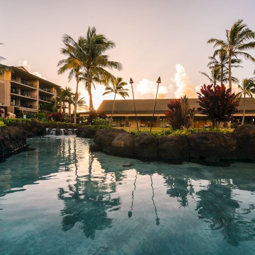 A resort pool surrounded by palm trees and buildings at sunset, creating a tranquil and tropical atmosphere.