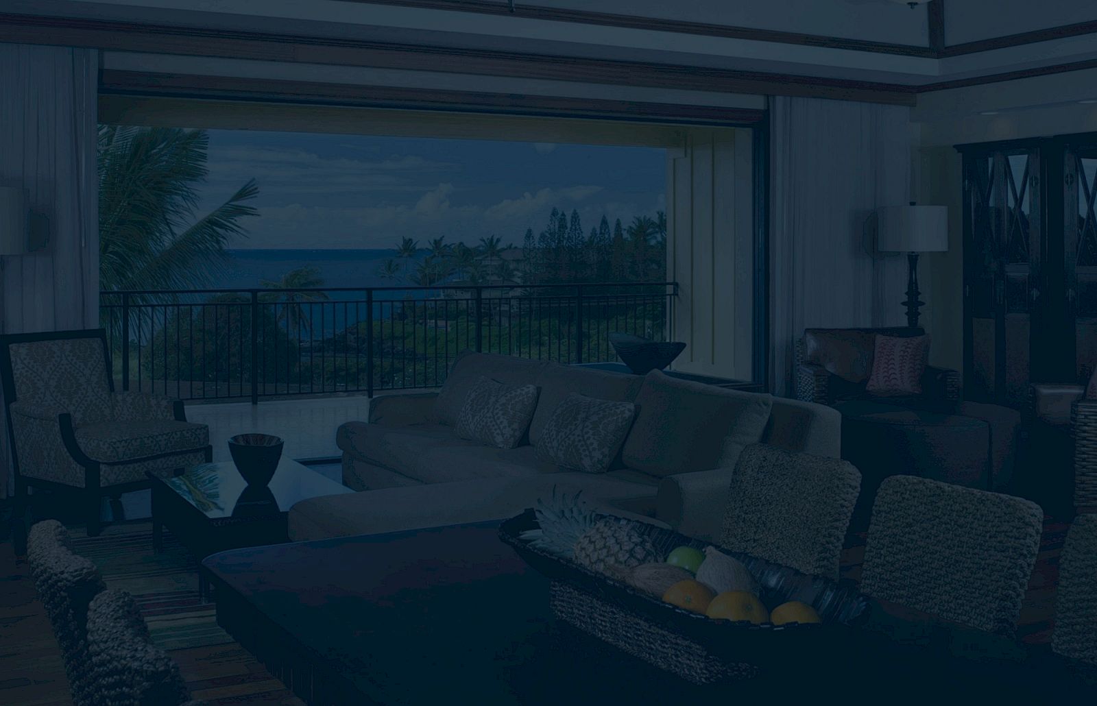 A cozy living room with wicker furniture opens to a balcony overlooking a tropical landscape and ocean view.
