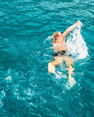 A person is swimming in a large body of water, with splashes around them, under clear blue skies.